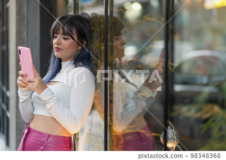 Serious woman using smartphone near glass wall Serious woman using smartphone near glass wall 98348368