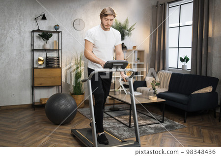 Full length portrait of young sportsman training home gym using treadmill. 98348436