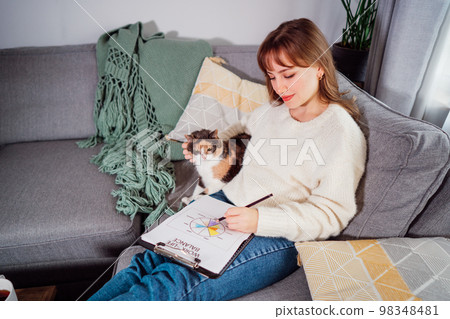 Relaxed young woman drawing work-life balance wheel sitting on the sofa with cat pet at home. Self-reflection and life planning. Coaching tools. Finding Balance in Your Life. Selective focus Relaxed young woman drawing work-life balance wheel sitting on the sofa with cat pet at home. Self-reflection and life planning. Coaching tools. Finding Balance in Your Life. Selective focus 98348481