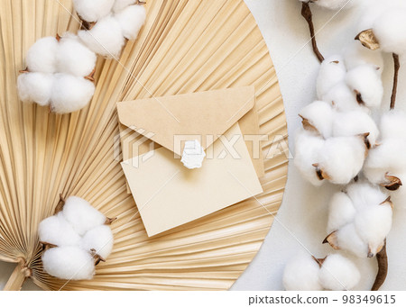 Blank card and envelope on dried palm leaf with cotton flowers top view, wedding mockup 98349615