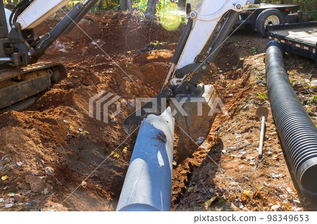 Worker who operate tractor lift sewage pipes in ground are preparing to install underground putting concrete pipes Worker who operate tractor lift sewage pipes in ground are preparing to install underground putting concrete pipes 98349653