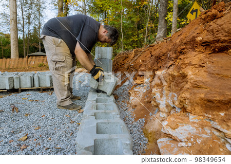 Construction worker was installing concrete block for retaining wall near new home in construction site Construction worker was installing concrete block for retaining wall near new home in construction site 98349654