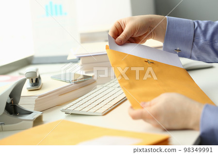 Businessperson opens yellow envelope with mail at workplace 98349991