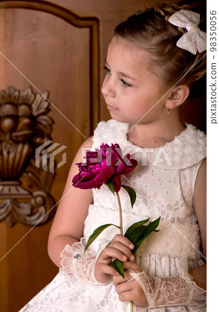 Children's holiday. Elegant girl in a white dress. Girl holding fresh peonies bouquet on wooden background 98350056