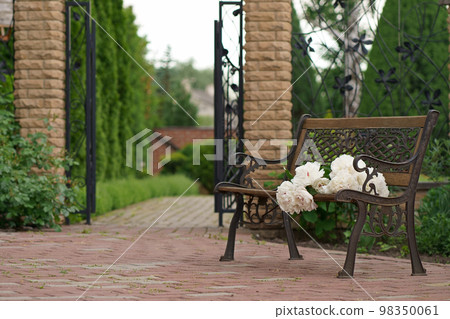 flower garden and vintage bench. A bouquet of peonies on a bench near a private house 98350061