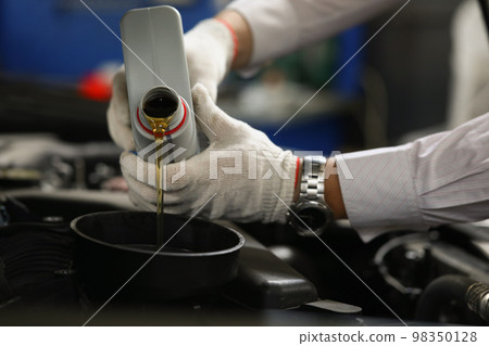 Hands of mechanic pours oil into car engine Hands of mechanic pours oil into car engine 98350128