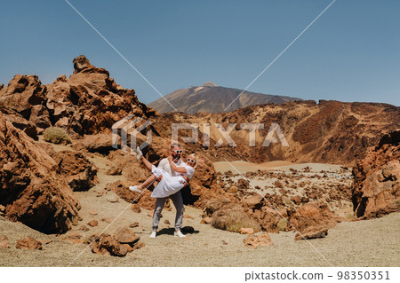 A married couple is standing in the crater of the Teide volcano. Desert landscape in Tenerife. Teide National Park. Tenerife, Spain A married couple is standing in the crater of the Teide volcano. Desert landscape in Tenerife. Teide National Park. Tenerife, Spain 98350351