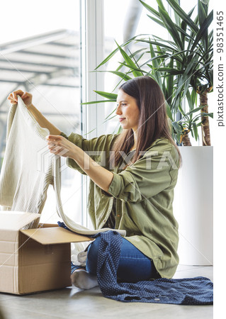 Vertical photo of a woman looking trough the clothes she bought online, taking them out of the box 98351465