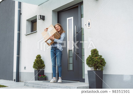 Happy young woman holding a cardboard box mailman just brought to her front door 98351501