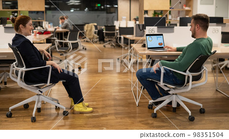 Redhead caucasian woman and bearded man are sitting on chairs in open space office.  98351504