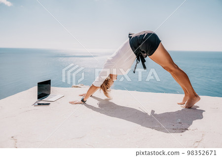 Woman sea laptop yoga. Business woman freelancer in yoga pose working over blue sea beach at laptop and meditates. Girl relieves stress from work. Freelance, digital nomad, travel and holidays concept 98352671