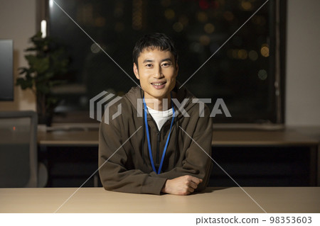 一個 30 多歲的男人晚上在辦公室裡看著相機 98353603