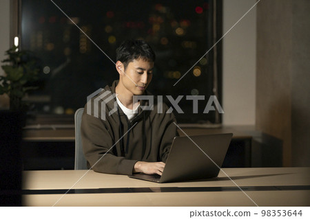 A man in his 30s working on a laptop, night office image A man in his 30s working on a laptop, night office image 98353644