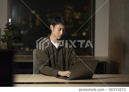 一個 30 多歲的男人在筆記本電腦上工作，夜間辦公室圖片 98353672