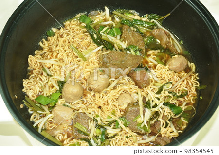 boiled instant noodles braised beef and meatball in black herb soup on electric cooking pot 98354545