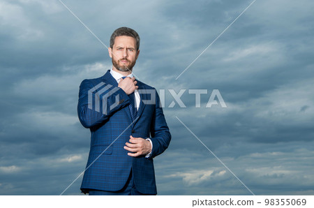 Grizzled guy in suit. Serious guy adjusting tie outdoors. Professional guy sky background Grizzled guy in suit. Serious guy adjusting tie outdoors. Professional guy sky background 98355069