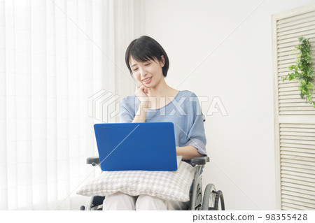 Disabled woman in a wheelchair using a computer at home 98355428