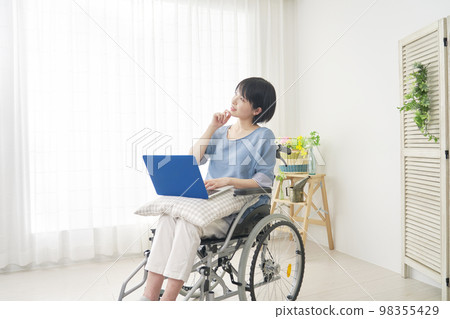 Disabled woman on a wheelchair imagining while using a computer at home 98355429