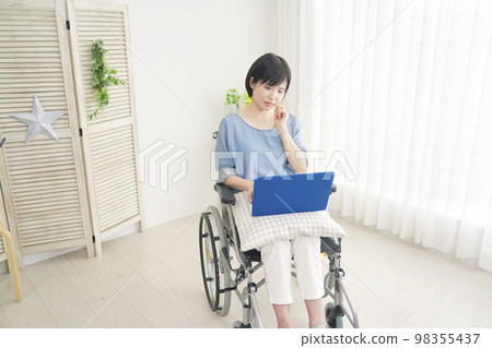 A disabled woman on a wheelchair who worries while using a computer at home A disabled woman on a wheelchair who worries while using a computer at home 98355437