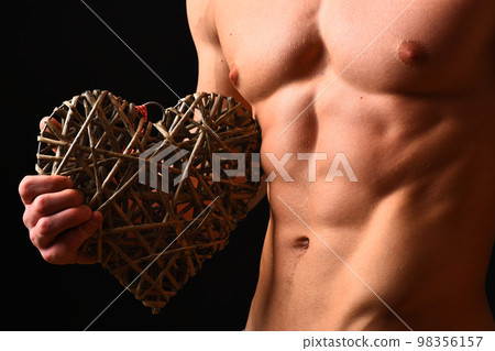 Athletes body in close up, hand holding big rattan heart Athletes body in close up, hand holding big rattan heart 98356157