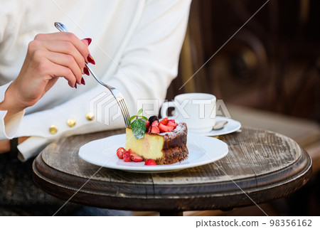 Cake with cream delicious dessert. Appetite concept. Dessert cake cup of coffee and female hand with fork close up. Piece of cake with red berry. Gourmet recipe food. Cake slice on white plate 98356162