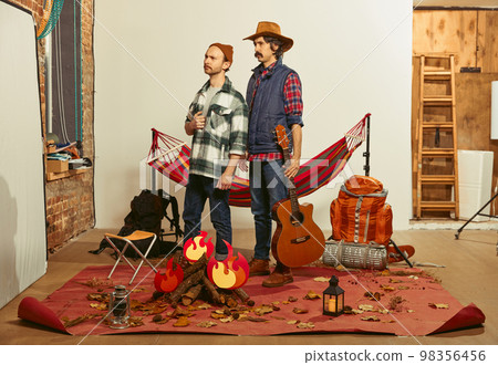 Serious, attentive look. Two men imagining, recreating camping activity indoors with necessary equipment. Concept of quarantine, travelling, imagination 98356456