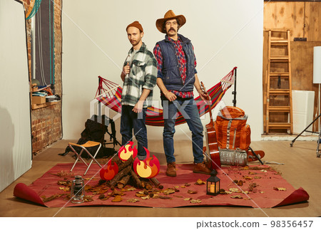 Friends, team. Two men imagining, recreating camping activity indoors with necessary equipment. Concept of quarantine, travelling, imagination Friends, team. Two men imagining, recreating camping activity indoors with necessary equipment. Concept of quarantine, travelling, imagination 98356457