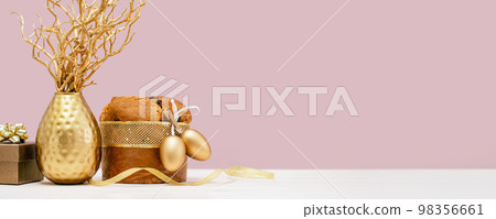 Happy Easter celebration banner. Italian Easter Decorated Panettone and golden eggs. tree branches in a vase and a gift box on white table. Festive setup decoration on tender pink. 98356661