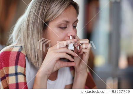 Sad woman with illness uses nasal spray while sitting at home close-up. 98357769