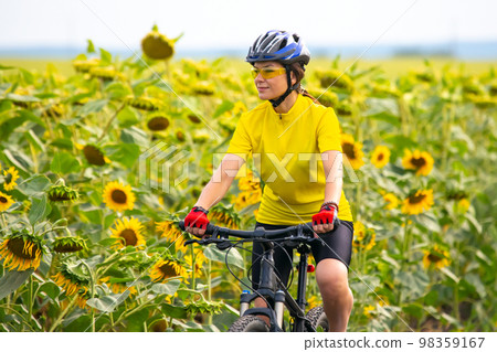 Beautiful woman cyclist rides a field with sunflowers on a bicycle. 98359167