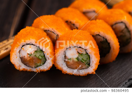 California sushi roll with salmon crab, cucumber and tobiko caviar served on black board close-up - Japanese food California sushi roll with salmon crab, cucumber and tobiko caviar served on black board close-up - Japanese food 98360495