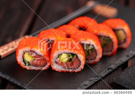 California sushi roll with salmon avocado, cucumber and tobiko caviar served on black board close-up - Japanese food California sushi roll with salmon avocado, cucumber and tobiko caviar served on black board close-up - Japanese food 98360499