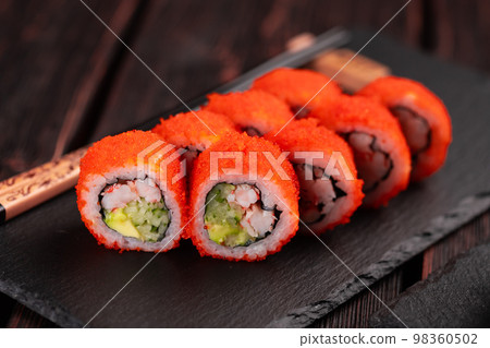 California sushi roll with crab, avocado, cucumber and tobiko caviar served on black board close-up - Japanese food California sushi roll with crab, avocado, cucumber and tobiko caviar served on black board close-up - Japanese food 98360502