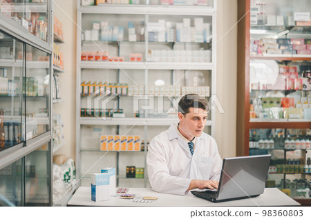 Male pharmacist checking, analyzing or Checks Inventory of Medicine, Drugs, Vitamins and checking prescription drugs for patients in modern pharmacy 98360803