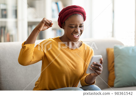Emotional african american woman using smartphone at home, gesturing 98361542