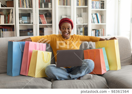 Happy black woman shopaholic sitting among purchases on couch 98361564