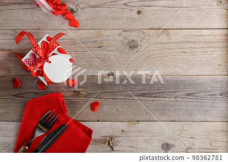 Valentines day dinner background with gift, cutlery with red hearts on wooden background. Romantic holiday table setting 98362781