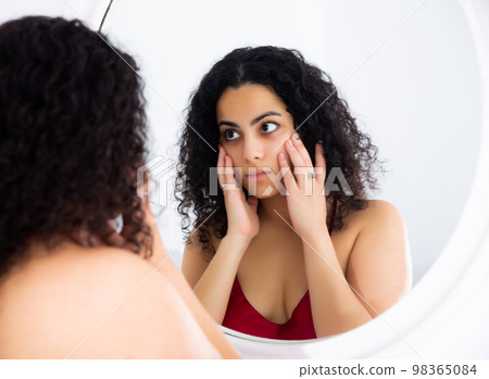 Woman checking her face in mirror in morning 98365084