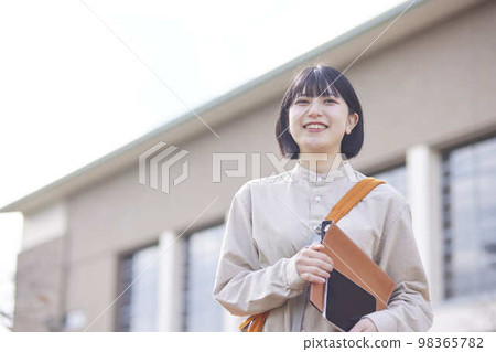 A young Japanese female student carrying a tablet and a bag on the university campus. A young Japanese female student carrying a tablet and a bag on the university campus. 98365782