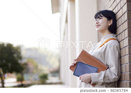 A young Japanese female student holding a tablet device in a university hallway. A young Japanese female student holding a tablet device in a university hallway. 98365784