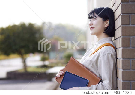 A young Japanese woman holding textbooks and a tablet in the school hall. A young Japanese woman holding textbooks and a tablet in the school hall. 98365786