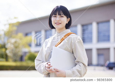 A young Japanese female university student walks around the school building with a laptop in her hand. A young Japanese female university student walks around the school building with a laptop in her hand. 98365800