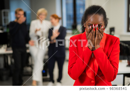 Young african woman crying because of the ridicule of colleagues. Racial discrimination in the office. Young african woman crying because of the ridicule of colleagues. Racial discrimination in the office. 98368541