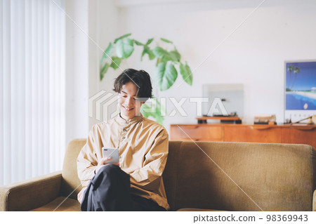 一個男人坐在沙發上，看著他的智能手機 98369943