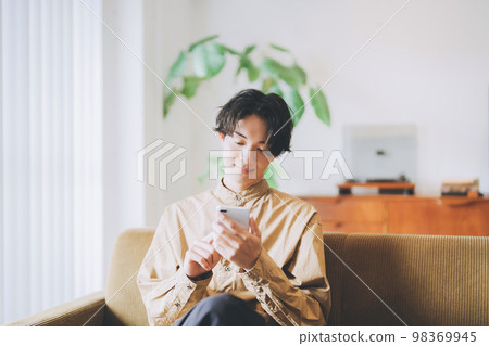 一個男人坐在沙發上，看著他的智能手機 98369945