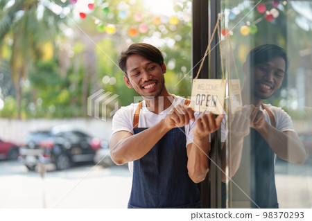 Young male manager in restaurant with tablet. Man coffee shop owner with open sign. Small business concept 98370293