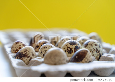 Spotted quail eggs in an egg box on a yellow background, natural eco friendly products. Spotted quail eggs in an egg box on a yellow background, natural eco friendly products. 98375940
