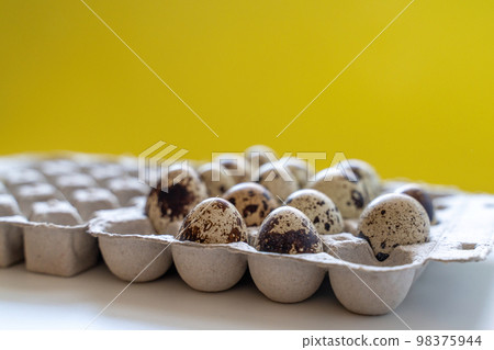 Spotted quail eggs in an egg box on a yellow background, natural eco friendly products. Spotted quail eggs in an egg box on a yellow background, natural eco friendly products. 98375944