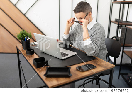 Business woman in the office sitting in front of a laptop looking at the screen Through glasses Business woman in the office sitting in front of a laptop looking at the screen Through glasses 98376752