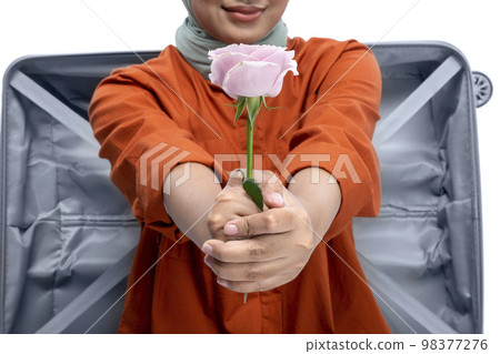 Asian Muslim woman in a headscarf sitting in a suitcase while holding a pink rose flower Asian Muslim woman in a headscarf sitting in a suitcase while holding a pink rose flower 98377276
